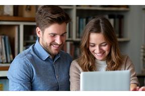 Un étudiant et un tuteur souriant travaillant ensemble sur des documents dans une bibliothèque confortable, représentant des leçons de français privées et personnalisées.
